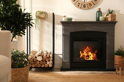 Bright beige modern room with a grey fireplace featuring a roaring fire, and a stack of birch logs placed to the side