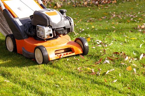 Sunny grass lawn with fall leaves being mowed by an orange lawnmower