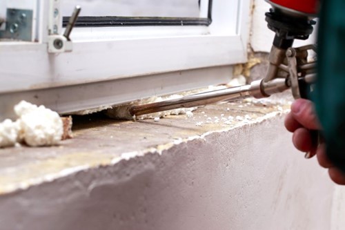 Close-up of gun spray foam sealant being applied to the gap on the underside of a window