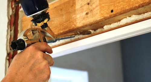 Close-up of a hand using a gun spray foam to fill the gap between a window and its frame.